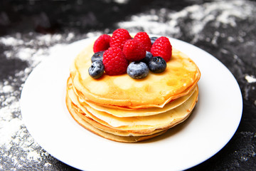 Image of plate with pancakes, blueberries, raspberries dusted with icing sugar.