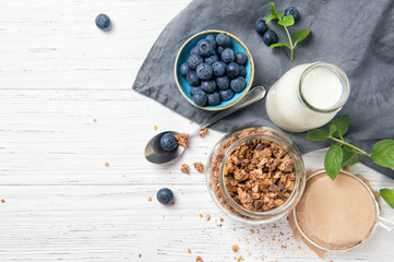 Fototapeta na wymiar Granola muesli, milk and ripe blueberries with mint leaves, healthy breakfast concept, wooden background, top view