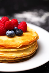 Closeup photo of plate of pancakes, blueberries, raspberries and powdered sugar.