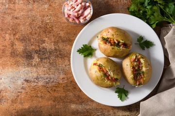 Stuffed potatoes with bacon and cheese on plate on rusty background. Top view