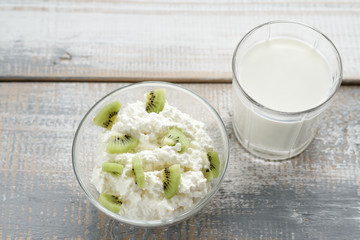 Cottage cheese with kiwi and a glass of milk on a white-gray wooden background