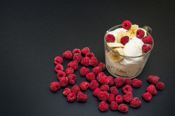 white ice cream in a transparent glass, with frozen raspberries and banana, on a black background