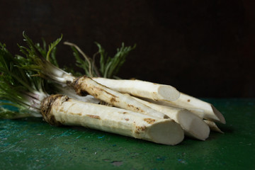 Fresh and grated horseradish in wooden bowl with leaves on green  cutting board.