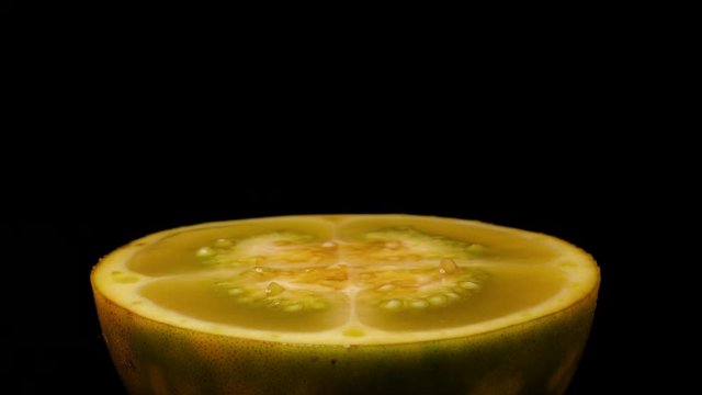 Close-up side view, solanum quitoense naranjilla fruit sliced in half slowly rotating on turntable isolated on black background.