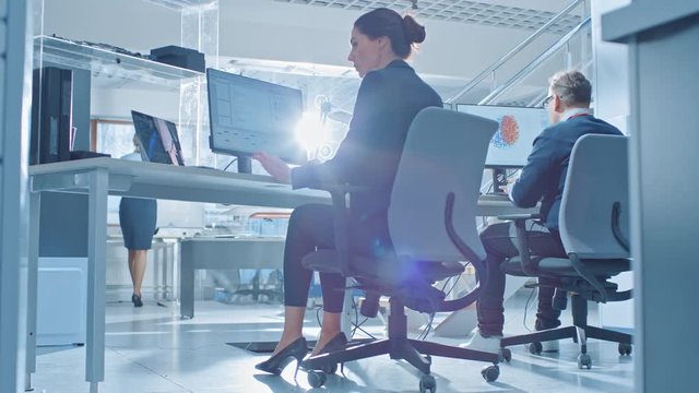 Back View of Team of Technology Engineers Working on Desktop Computers in Bright Office. Screens Show IDE / CAD Software, Implementation of Machine Learning, Neural Networking and Cloud Computing
