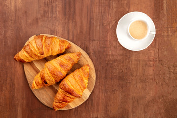 A breakfast with croissants and coffee, shot from the top forming a frame on a dark rustic wooden background with a place for text