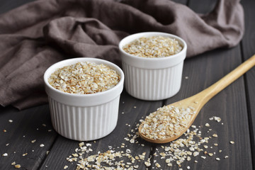 Rolled oats in bowls and spoon on dark wooden table background