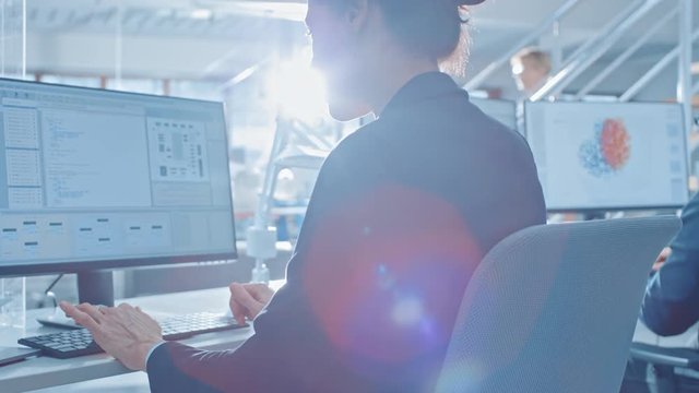 Back View of Team of Technology Engineers Working on Desktop Computers in Bright Office. Screens Show IDE / CAD Software, Implementation of Machine Learning, Neural Networking and Cloud Computing