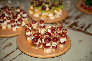 Grape with cheese canapes on a round wooden plate