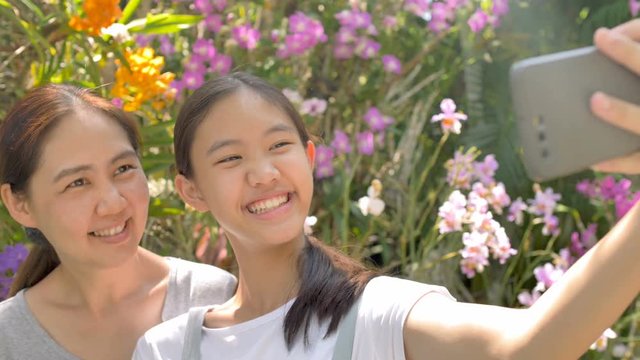 Happy Asian girl and mother enjoying blooming flowers and take a photo together, Slow motion shot