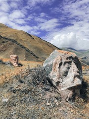 The meadow at the mountain foot in Sno village with the boulders with carved faces of famous Georgian cultural figures. The stone heads of famous writers poets on the on the autumn countryside Kazbegi