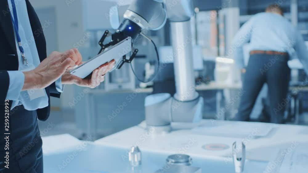 Leinwandbilder Stylish Female Industrial Robotics Engineer Uses Tablet Computer to Program and Manipulate Robot Arm for Lifting, Moving Objects. Technology Research Facility for Machine Learning and Cloud Computing