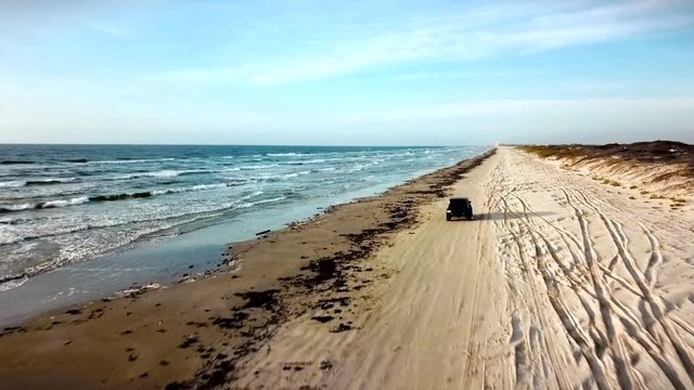 Drone footage of Jeep Wrangler driving along coast