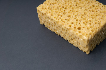 Close up view of cleaning sponge, mesh structure pattern on black surface. Yellow sponge close-up.