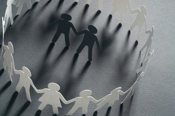 Paper figure of a male couple surrounded by circle of paper people holding hands on gray background. Minorities, bulling, diversity concept.