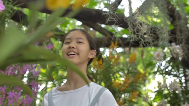 Happy Asian girl enjoying blooming flowers in summer garden at sunny day, Slow motion shot