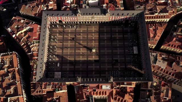 The Plaza Mayor in Madrid in an aerial shot. Teh camera rises and flys backwards on a sunny day. The roofs of Madrid can be seen from above.