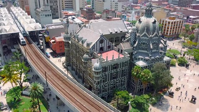Stunning aerial 4k shot of Plaza Botero and moving metro train on railway surrounded with palms