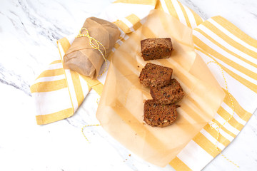 Homemade Zucchini Bread; One Loaf Sliced on Parchment Paper; Second Loaf Wrapped in Parchment Paper; Yellow and White Dish Towel; Marble Countertop
