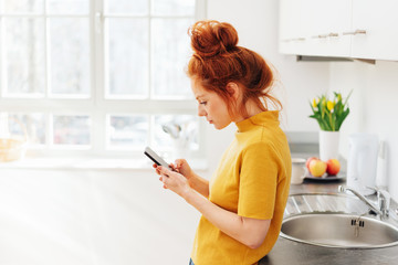 Woman with smartphone, leaning on kitchen sink