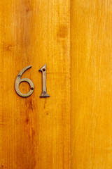 House number 61 with the sixty-one in bronze numbers on a varnished light wooden door with visible grain