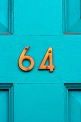 House number 64 with the sixty-four in bronze metal on the middle cross of the wooden panel on the turquoise wooden house door