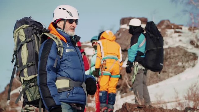 an adult climber is a man who looks into the distance with a serious face and turns to the camera. in the background is his team, which is waiting for their forerunner.