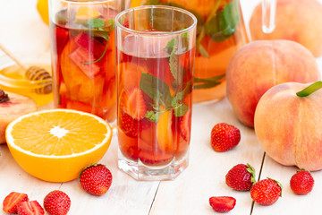 Glass of strawberry soda drink. Summer refreshing drinks, fruit and berry raspberry mojito or lemonade with fresh mint, peach, strawberry, slices of orange, lemon and honey on a light background.