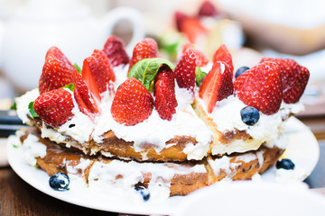 Strawberry cake in cream and mint leaves on the table in a plate, on the background of a teapot with tea, in light colors, close-up with a blurred background.