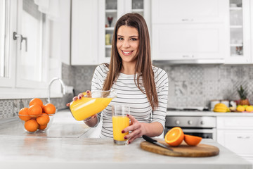 Beautiful young woman preparing fresh juice in kitchen. Looking at camera.