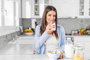 Smiling woman drinking a large glass of milk while eating a cereals for breakfast