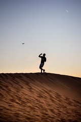 Dark silhouette of a man walking at the desert dunes. Dawn time