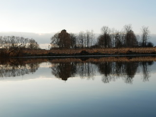 Fototapeta premium Polonne / Ukraine - 18 February 2019: Scenic river reflections of trees on the water. A river with trees on the shores. Reflection of blue sky with clouds in calm water