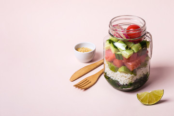 Hawaiian salmon poke salad in glass jar with rice and vegetables on pink background