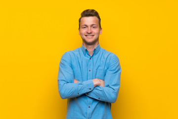 Blonde man over isolated yellow wall keeping the arms crossed in frontal position