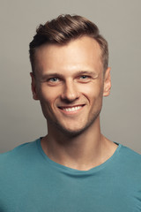Obraz premium Male beauty, boy next door concept. Portrait of smiling 30-year-old man standing over gray background. Close up. Classic style. Wavy glossy blond hair. Studio shot