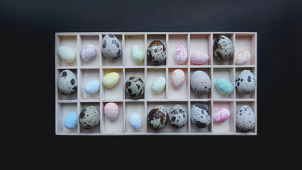 Quail eggs and easter eggs in wooden containers. Top view. Black background