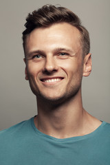 Obraz premium Male beauty, boy next door concept. Portrait of smiling 30-year-old man standing over gray background. Close up. Classic style. Wavy glossy blond hair. Studio shot