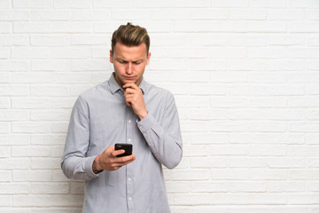 Blonde man over white brick wall thinking and sending a message