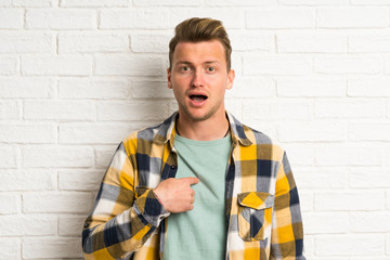 Blonde handsome man over white brick wall with surprise facial expression