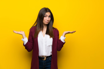 Young woman over yellow wall having doubts while raising hands