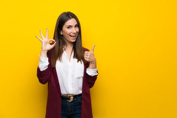 Young woman over yellow wall showing ok sign with and giving a thumb up gesture - obrazy, fototapety, plakaty