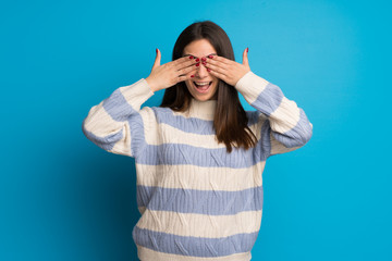 Young woman over blue wall covering eyes by hands. Surprised to see what is ahead