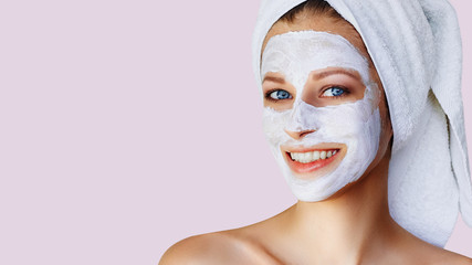 Beautiful young woman with facial mask on her face. Skin care and treatment, spa, natural beauty and cosmetology concept.