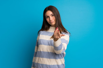 Young woman over blue wall inviting to come with hand. Happy that you came