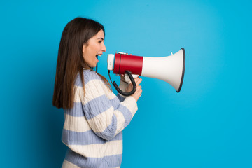 Young woman over blue wall shouting through a megaphone