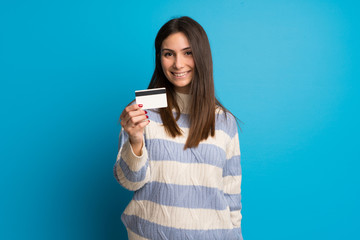 Young woman over blue wall holding a credit card