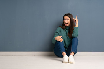 Young woman sitting on the floor pointing up and surprised