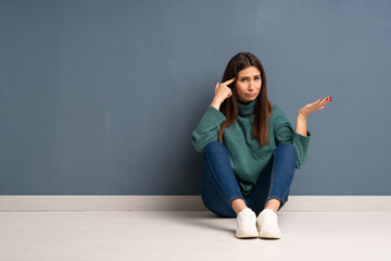 Young woman sitting on the floor making the gesture of madness putting finger on the head