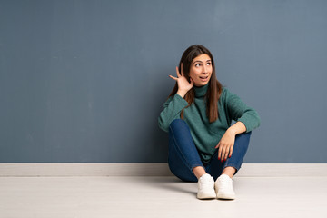 Young woman sitting on the floor listening to something by putting hand on the ear